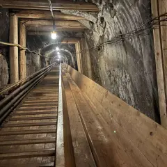Długi, drewniany tunel w kopalni w Krakowie, oświetlony lampami, prowadzi w głąb ziemi.