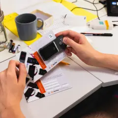 Ręce trzymają alkomat i certyfikat kalibracji. Na stole sprzęt laboratoryjny, baterie i kubek. Dowiedz się, ile trwa kalibracja alkomatu.