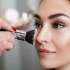 Mano con pennello applica terra sul viso per un look naturale.