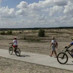 Ludzie na rowerach i pieszo na ścieżce rowerowej w krajobrazie pustynnym.