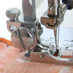 Close-up of a sewing machine needle and blind hem foot working on orange fabric. Learn how to use blind hem foot for invisible hems.