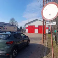 Znak zakazu wjazdu i samochód Dacia przed remizą OSP. Czy wjazd pod zakaz tonażowy grozi mandatem i punktami?