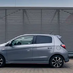Szary Mitsubishi Space Star stoi na tle nowoczesnej, szarej ściany z poziomymi żaluzjami.