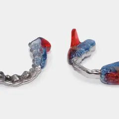 Dos aparatos mandibulares transparentes con detalles en rojo y azul, uno con una banda metálica.