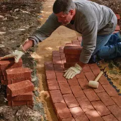Man laying red bricks to create a new brick walkway in a garden.