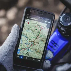 Rękawica trzyma smartfon z aplikacją szlaki turystyczne Locus Map Pro, pokazującą trasę w górach.