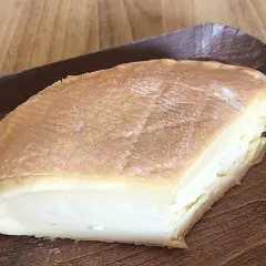 Un morceau de fromage à pâte molle, à la croûte orangée et à l'odeur prononcée, servi sur un plateau en bois.