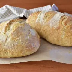 Due pagnotte di pane morbido fatto in casa, dorate e leggermente infarinate, su carta da forno.