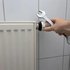 Dłoń z kluczem nastawia termostat, pokazując, jak spuścić wodę z kaloryfera.