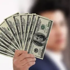 Dłoń trzyma wachlarz banknotów 100 dolarowych, symbolizujących sposób, jak płacić czynsz za mieszkanie.
