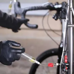 Hands in black gloves perform a bike brake bleed, following the correct brake bleed order to ensure optimal performance.
