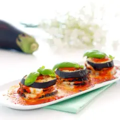 Deliciosas berenjenas a la parmesana, apiladas y cubiertas de salsa de tomate y queso fundido, adornadas con albahaca fresca.