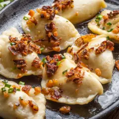 Pyszne pierogi z mięsem, okraszone skwarkami i szczypiorkiem, podane na żeliwnej patelni.