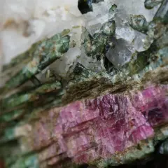 Zielony turmalin właściwości: kryształy o barwie zieleni i różu, z widocznymi inkluzjami, tworzące naturalną formację skalną.
