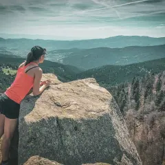 Une randonneuse admire le paysage depuis un rocher. Une parfaite destination randonnée pour s'évader.