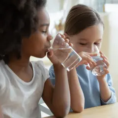 Deux enfants, une fille noire et une fille blanche, boivent de l'eau à la même table. L'eau est essentielle pour chaque enfant.