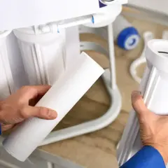 Main tenant d'un filtre, un homme prépare l'entretien de son osmoseur.