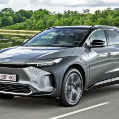 Szary Toyota bz4x cena jest atrakcyjna, gdy jedzie nad jeziorem.