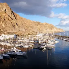 El puerto deportivo Aguadulce, con sus barcos amarrados y un hotel blanco, se extiende bajo una imponente montaña rocosa.