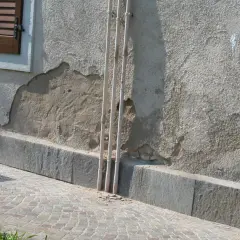 Il muro esterno grezzo mostra scrostamenti e necessita di essere pitturato. Tre tubi bianchi corrono verticalmente lungo la parete.