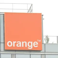 Pomarańczowy znak z napisem "orange" na nowoczesnym budynku. To logo firmy telekomunikacyjnej, która oferuje usługi multiroom.