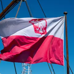Flaga bandery w Polsce, biało-czerwona z orłem, powiewa na maszcie żaglowca na tle błękitnego nieba.