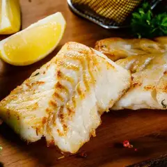 Filetti di branzino in padella in bianco, dorati e succulenti, serviti con spicchi di limone fresco e insalata croccante.
