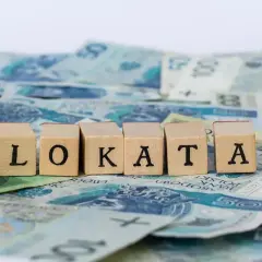 Drewniane klocki z literami "LOKATA" na tle polskich banknotów.