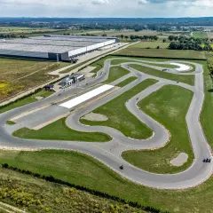Asfaltowe tory wyścigowe w Polsce, otoczone zielenią i polami, z widocznym budynkiem zaplecza i kilkoma motocyklistami.