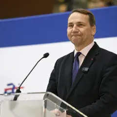 Mężczyzna w garniturze, podobny do Jana Sikorskiego, ojca Radosława Sikorskiego, przemawia przy mównicy.