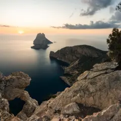 Vista del ojo de es Vedrà al atardecer, con el sol poniente tiñendo el cielo de naranja y el mar en calma.