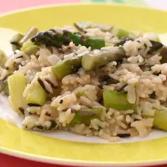Pyszne risotto ze szparagami, z dodatkiem dzikiego ryżu, na żółtym talerzu.
