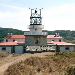 El faro de estaca de bares se alza imponente sobre la costa, con sus edificios blancos y tejados rojos rodeados de vegetación.