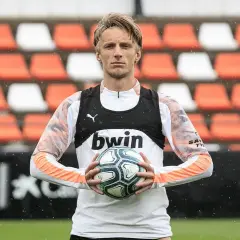 Piłkarz z blond włosami trzyma piłkę, ubrany w białą koszulkę z pomarańczowymi rękawami i czarną kamizelkę z logo bwin. W tle pomarańczowo-białe trybuny.