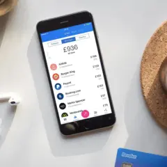 Telefon z aplikacją Revolut pokazuje transakcje, ułatwiając zrozumienie, jak płacić Revolutem za granicą. Obok leżą słuchawki i karta.