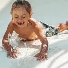 Enfant riant sur un toboggan aquatique, éclaboussures d'eau. Attention aux otites du baigneur symptômes après ces jeux !