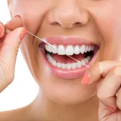Donna sorride mentre usa il filo interdentale cerato per pulire i suoi denti bianchi e sani.