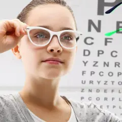 Dziewczynka w białych okularach przymierza okulary na tle tablicy Snellena.