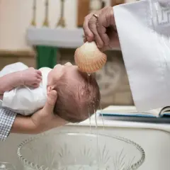 Un bébé est baptisé dans une église, l'eau bénite coule de la coquille sur sa tête. Un moment solennel pour qui inviter à un bapteme.