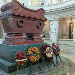 Imponujący sarkofag Napoleona, otoczony rzeźbami i wieńcami, w monumentalnym wnętrzu.
