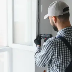 Fachowiec reguluje okno wiertarką. Dowiedz się, ile kosztuje wyregulowanie okna, aby zapewnić jego prawidłowe działanie.