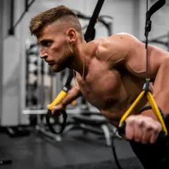 Mężczyzna wykonuje pompki z użyciem taśm TRX. Intensywny trening okluzyjny buduje siłę i masę mięśniową.