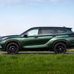 Zielony Toyota Highlander z czarnymi felgami stoi na tle pól i nieba.