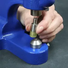 Dłoń przygotowuje element do rozwiercania nitów za pomocą niebieskiej prasy.