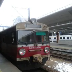 Pociąg ED72-013 ra stoi na peronie. W tle widać nowoczesny budynek dworca i inne pociągi.