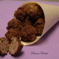 Un cono di carta pieno di polpette fritte dorate, una tagliata a metà rivela un interno succoso.