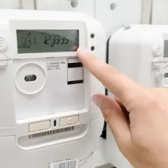 Palec naciska przycisk licznika energii elektrycznej, monitorując pobór prądu.