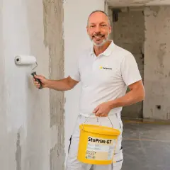 Maler trägt eine Grundierung auf eine Wand auf. Für Rollputz ist eine Grundierung notwendig, um ein optimales Ergebnis zu erzielen.