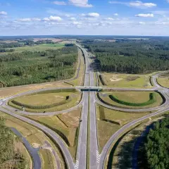 Nowa droga ekspresowa, idealna trasa do Kołobrzegu, przecina lasy i pola. W oddali widać farmę wiatrową.