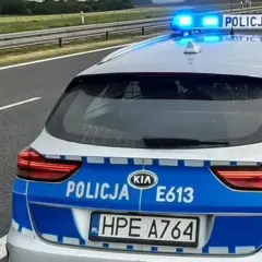 Policyjny pojazd uprzywilejowany z włączonymi niebieskimi światłami stoi na poboczu autostrady.